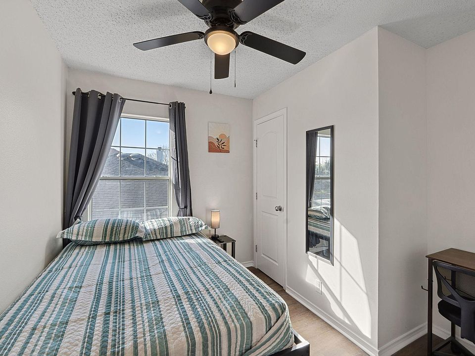 Bedroom with comfortable bed, a mini fridge, a TV, and a work desk. A mini closet & a ceiling fan.