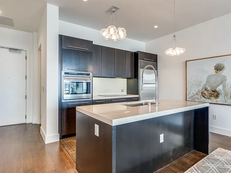 Kitchen featuring modern cabinets, hanging light fixtures, oven, dark wood finished floors, and a kitchen island with sink