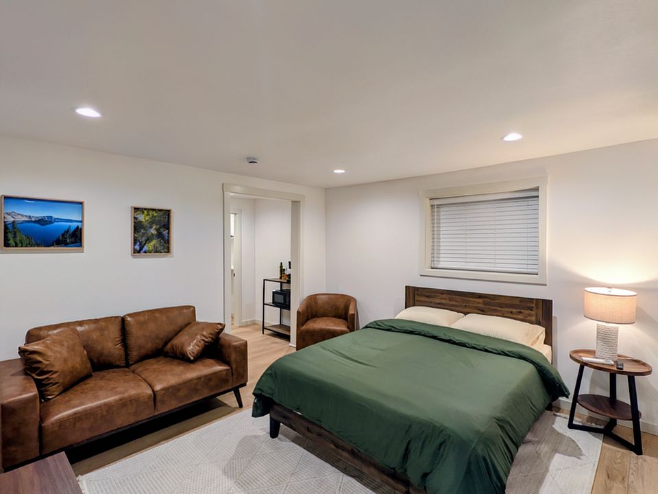 Unit 7 comes furnished with a queen size bed, a small couch, a swivel lounge chair, a dedicated workspace, and a night stand with a lamp. Flooring in the room is LVP.