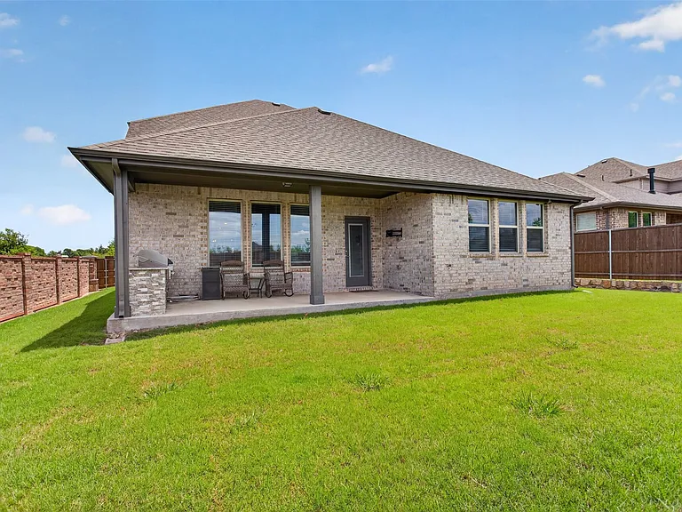 Expansive backyard featuring a covered patio with brick columns, a built-in stone grill station, and a concrete patio surface