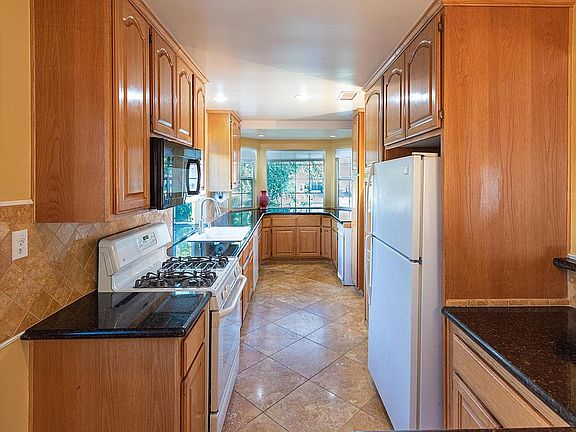 Kitchen with granite counters and travertine floors. Refrigerator, gas stove/oven, trash compactor, dishwasher, built-in microwave.
