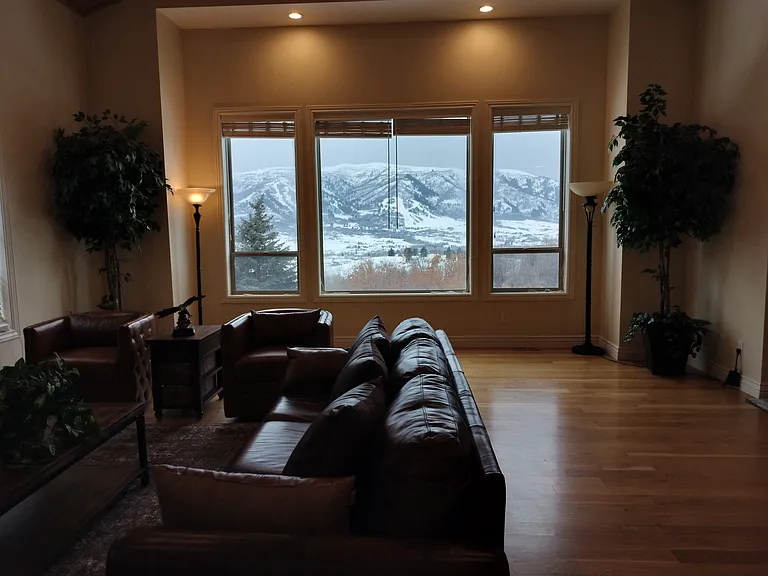 Stunning mountain views of Nordic Valley Ski Resort from your spacious living room. This inviting space features large windows for natural light, a cozy fireplace, recessed lighting, and a ceiling fan, creating the perfect atmosphere for relaxation.