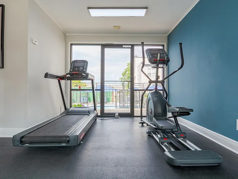 A treadmill and elliptical are shown looking out of floor to ceiling windows in the fitness center at ReNew on Cantrell.