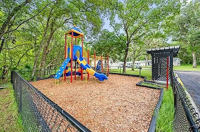 Inviting playground area with colorful slides and climbing structures in a serene, fenced park setting.
