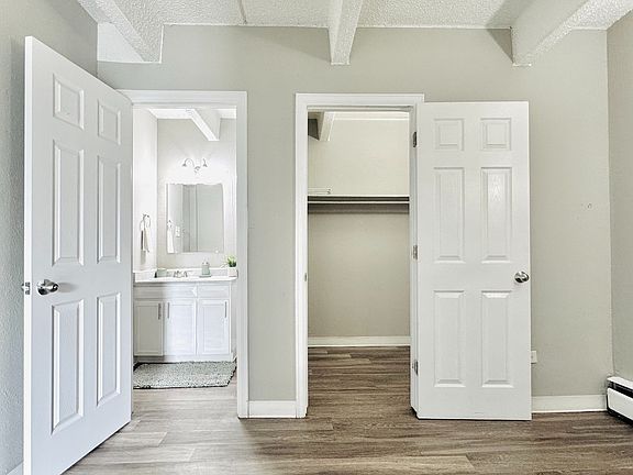 Bright and inviting bedroom featuring an open door leading to a modern bathroom, ample closet space, and elegant hardwood flooring.