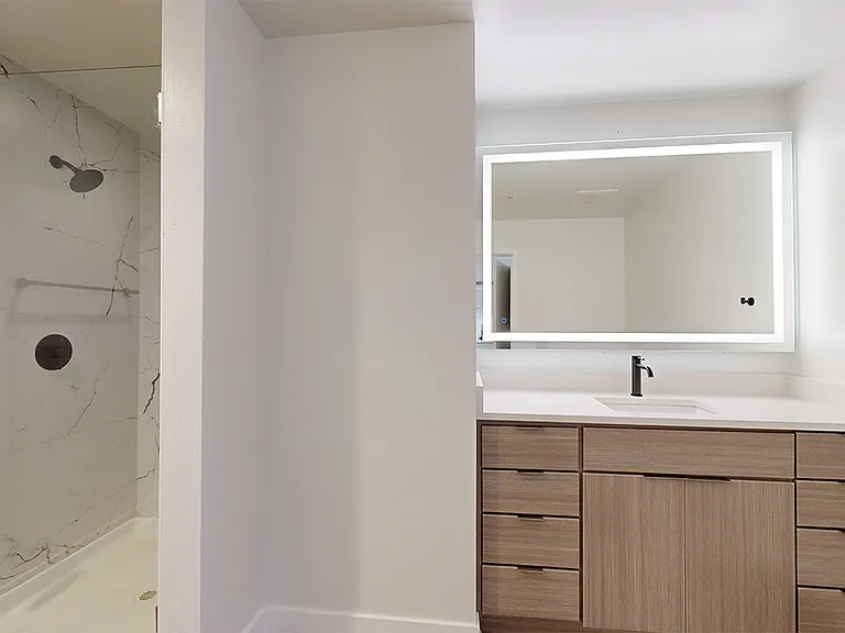 Apartment bathroom with glass enclosed shower, wood-style flooring, and LED vanity mirror.