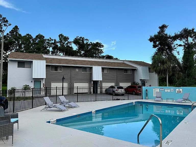 Inviting apartment complex with a pristine swimming pool, lounge chairs, and modern architecture set against lush greenery.