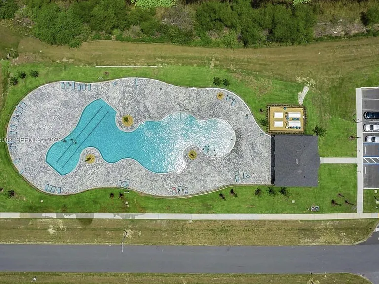 Resort-style community pool with expansive sundeck seating, plus adjacent parking and a shaded pavilion area.