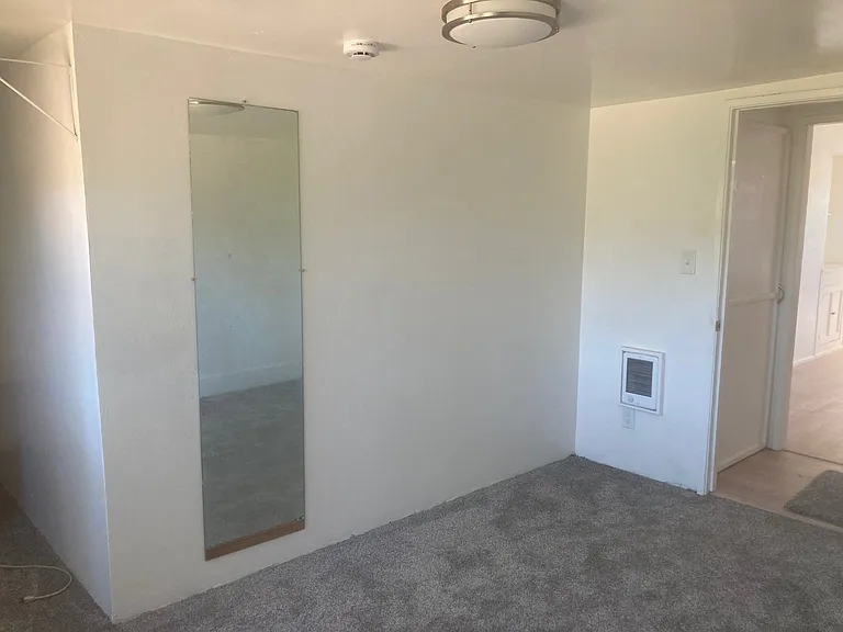 The view towards the kitchen in the smaller bedroom. The full length mirror can be seen as well as the heater vent to the right of the door