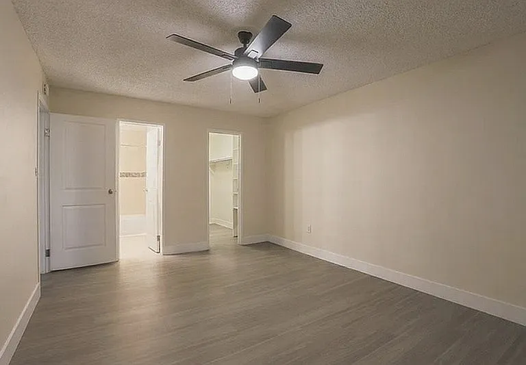 Inviting bedroom with sleek hardwood flooring, modern ceiling fan, and walk-in closet access, exuding comfort and style.