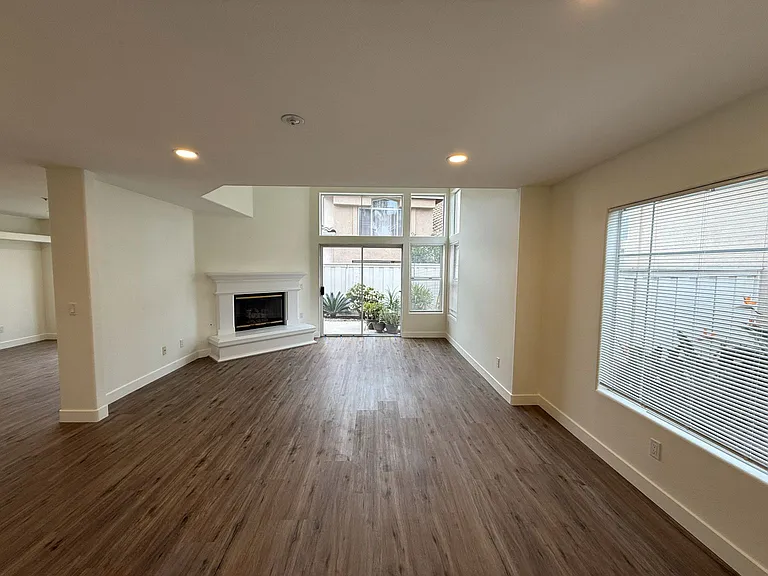 Spacious, light-filled living room featuring a gas fireplace, recessed lighting, new flooring, and fresh paint.