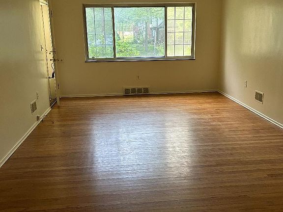 The living room is spacious and has a large window for natural light as well as hardwood flooring.