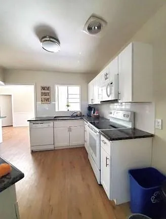 Galley kitchen with ample white cabinetry, full appliance suite, and durable counters, opening to an adjacent living area.