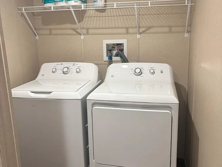 Dedicated laundry nook with full-size washer and dryer plus an overhead wire shelf for supplies and extra storage.