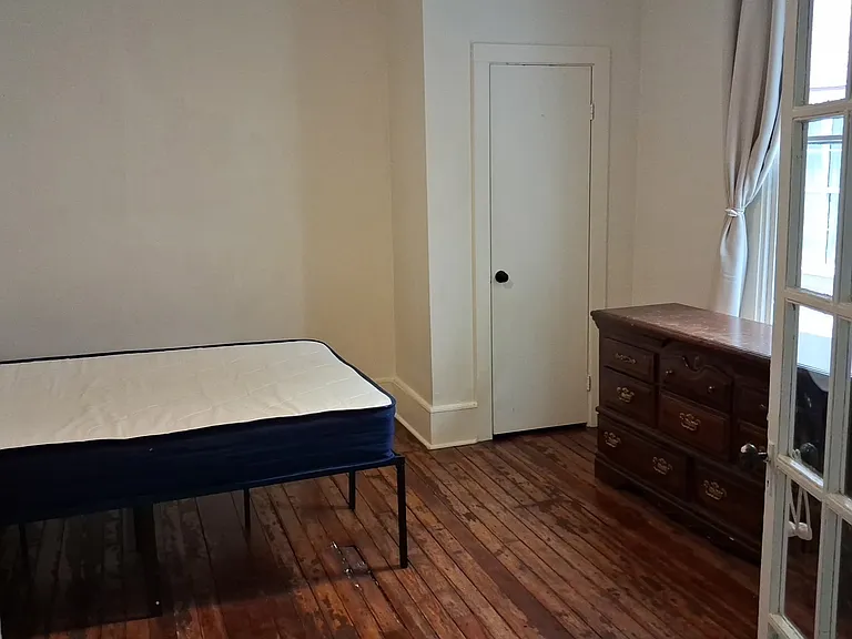 Available furnished bedroom with french doors and original decorative fireplace.