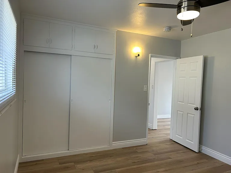 View from inside bedroom with side window on left, closets and brand new designer laminate floors, blinds, ceiling lamp/fan, wood molding and specialty paint.