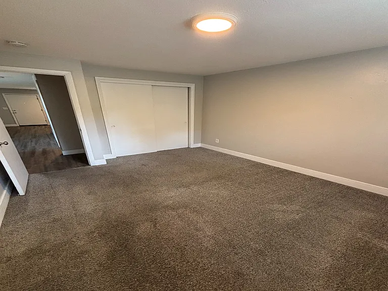 Inviting bedroom with plush carpet flooring, soft neutral walls, and sliding closet doors, perfect for a cozy retreat.