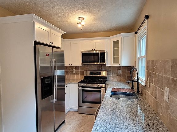 Shiny stainless steel appliances and countertops in the kitchen. The garage entry is the door to the left, where you will find laundry hookups. To the right is a door leading to the back porch area.