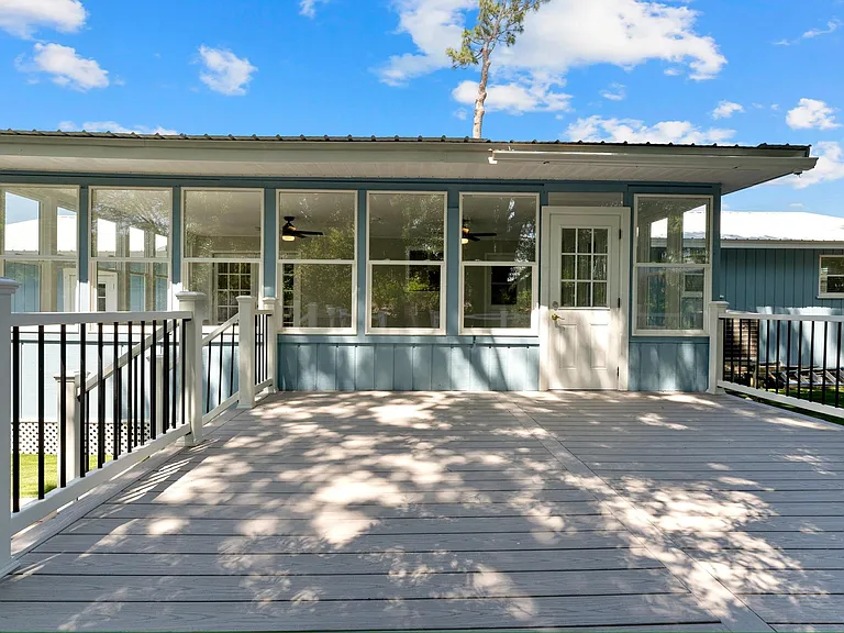 Elevated front deck with railings leads to a sunroom-style entry with large windows and a glass-panel door.