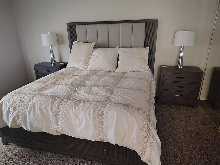 Spacious bedroom featuring a large bed with upholstered headboard, matching nightstands, and bedside lighting.