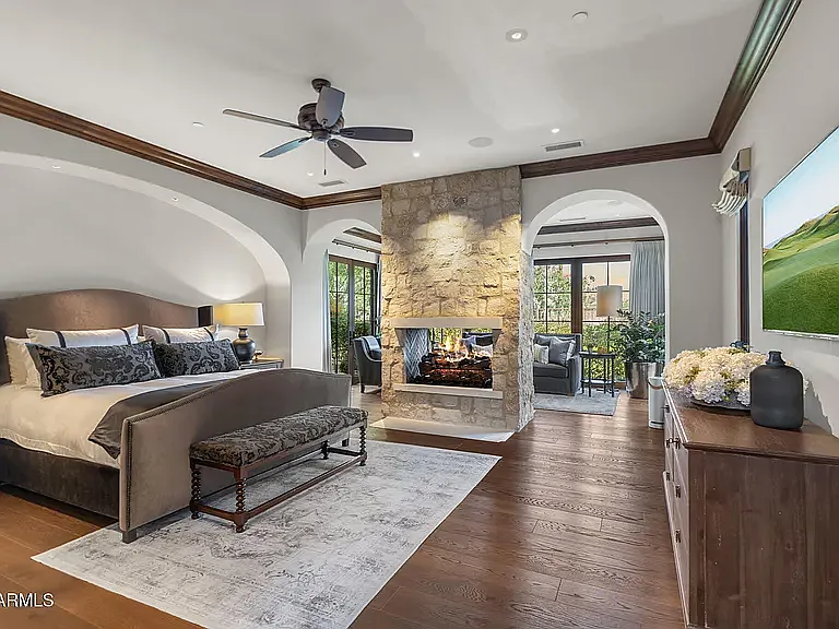 Spacious primary bedroom featuring a statement stone fireplace, elegant architectural archways, and a private sitting area.