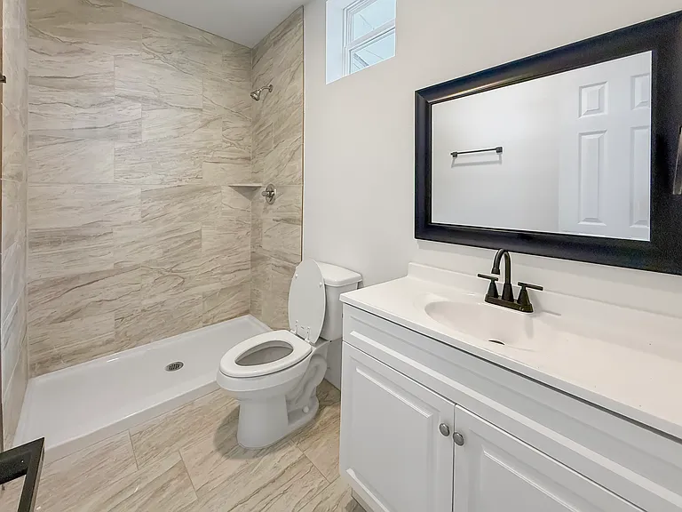 This bathroom features a modern shower with elegant gray tile, a sleek white vanity with a black-framed mirror, and contemporary fixtures, creating a clean and inviting space.