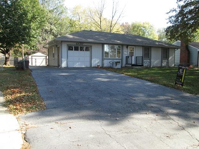 Front view of home with large driveway and metal shed in the bac