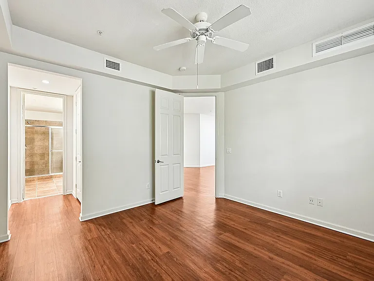 Modern apartment room with wooden flooring, a ceiling fan, and an en-suite bathroom featuring elegant tile work.