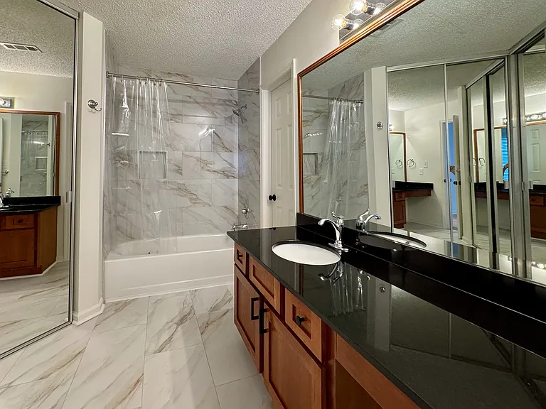 spacious en-suite bathroom with new tile, big vanity, and large walk-in closet with mirrored doors
