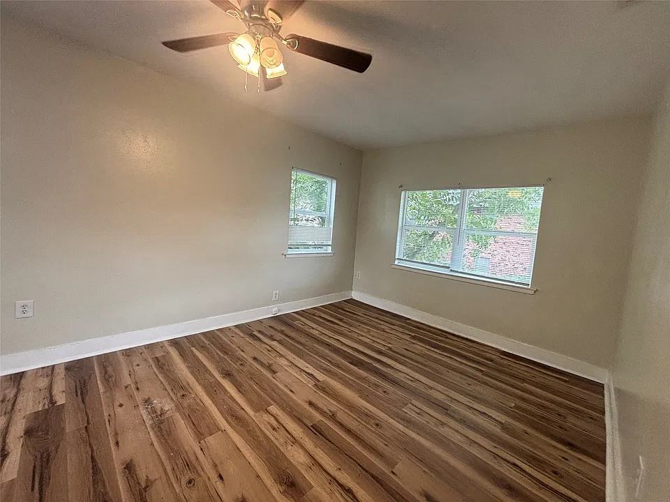 Wood-finish flooring with light-toned walls, featuring two windows and a ceiling fan with integrated lighting