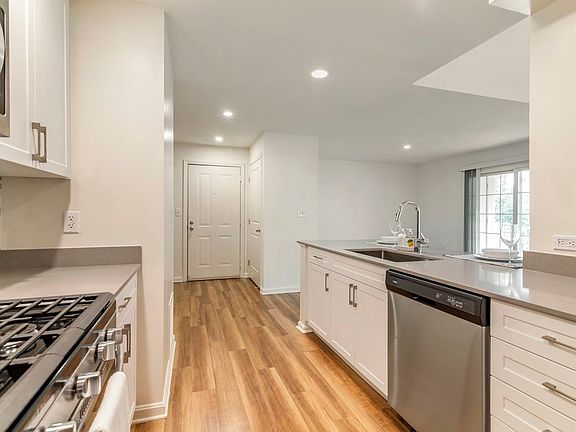 Renovated Package I kitchen with white cabinetry, grey quartz countertops, grey tile backsplash, stainless steel appliances, and hard surface plank flooring