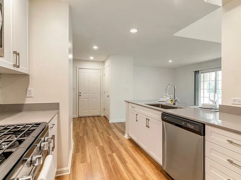 Renovated Package I kitchen with white cabinetry, grey quartz countertops, grey tile backsplash, stainless steel appliances, and hard surface plank flooring