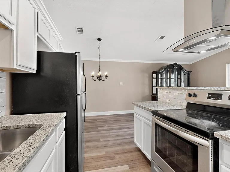 Kitchen with stainless steel appliances, white cabinetry, range hood, ornamental molding, and a chandelier