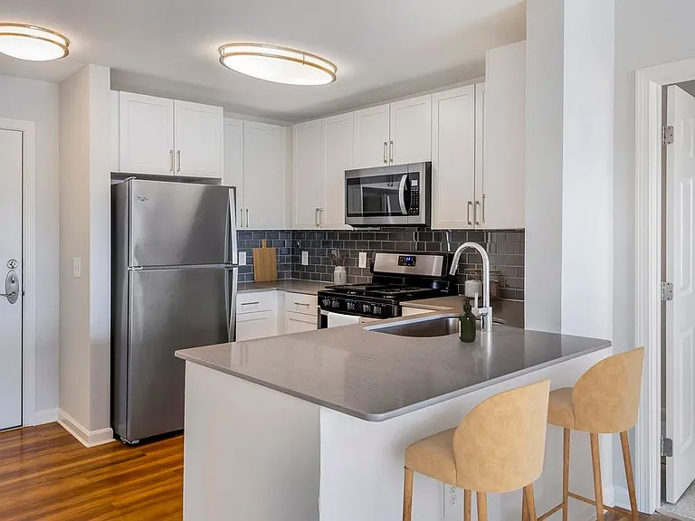 Renovated Package I kitchen with white cabinetry, grey quartz countertops, dark grey subway tile backsplash, stainless steel appliances, and hard surface flooring