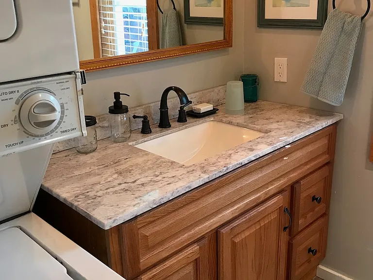 Bathroom with stacked washer/dryer, granite countertop and large mirror. Equipped with hand soap, bar soap, toothbrush holder and cups.