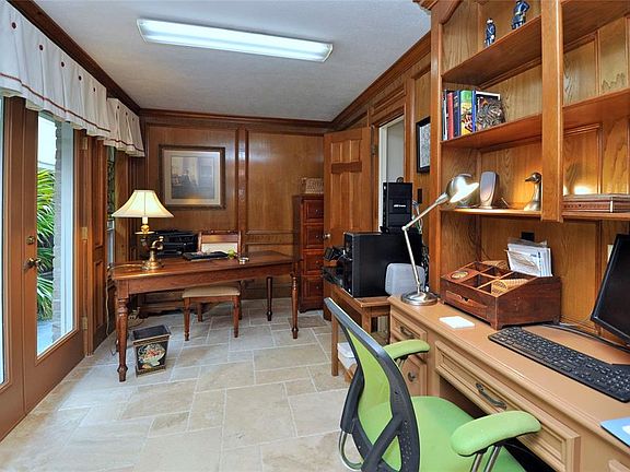 Handsome office overlooks the back patio and yard. Classic block paneling, built-in desk and shelves and the upgraded travertine Versailles pattern floor continued into here from the family room.