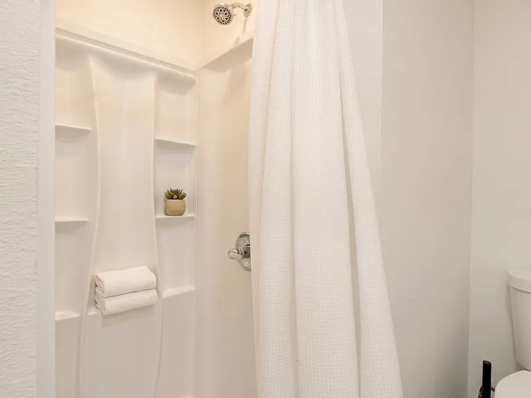 Clean shower/tub combo with built-in shelving for toiletries, plus a nearby toilet in a simple, easy-care bath layout.