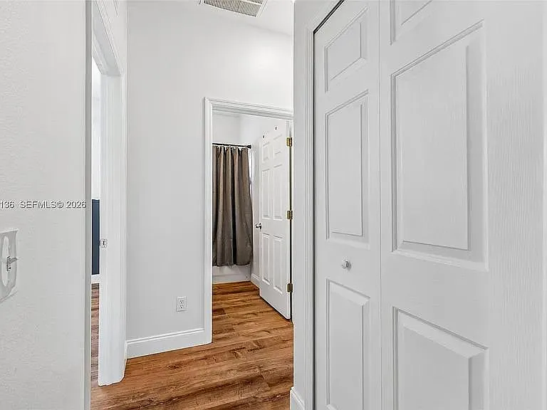 Interior hallway with wood-look flooring and multiple closets provides convenient storage and access to nearby rooms.