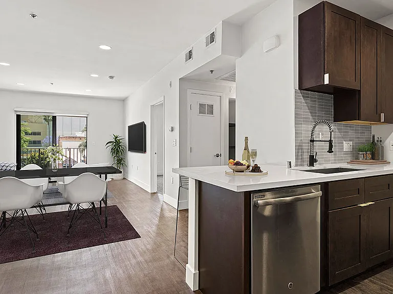 Tiled kitchen with stainless steel appliances and view of hardwood floored living room and balcony.
