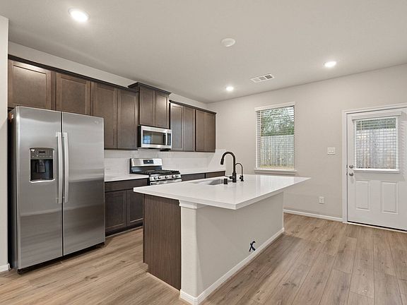 This light and bright kitchen features a large quartz island, dark stained cabinets, a large sink ov