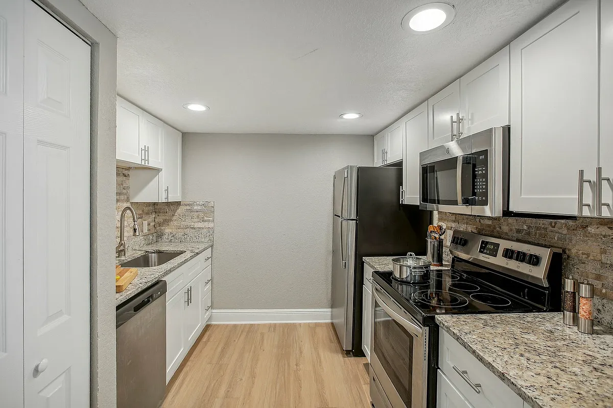 Modern kitchen with sleek stainless steel appliances, elegant granite countertops, and white cabinetry for a contemporary style. - Seastone Apartments