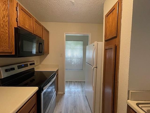 Kitchen featuring electric range, black microwave, freestanding refrigerator, brown cabinetry, and light wood-type flooring