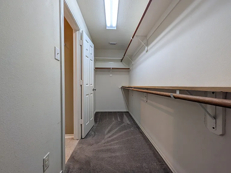 A spacious walk-in closet offering multi-level built-in hanging rods, upper storage shelving, carpeted flooring, and plenty of room to organize your wardrobe.
