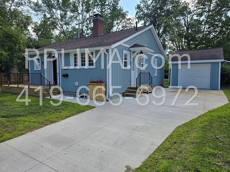 Striking cobalt blue board-and-batten siding with brand new windows, concrete driveway, and detached