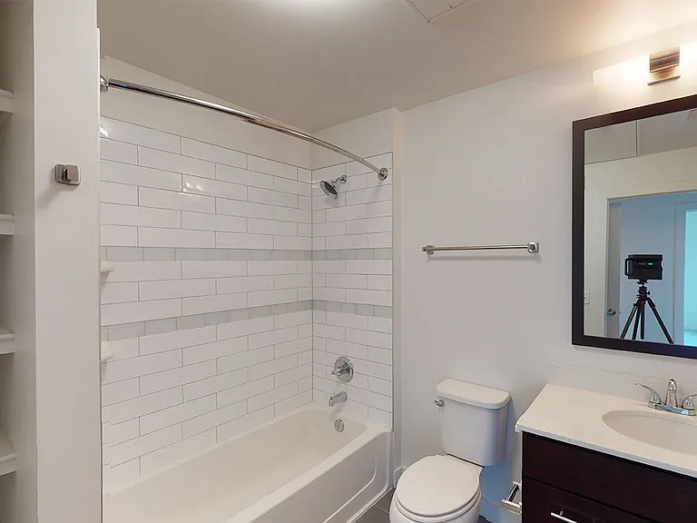 Apartment bathroom with white tiled shower and dark wooden cabinets.