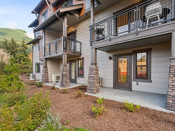 A multi-story residential building with balconies, surrounded by landscaped greenery and a mountaino