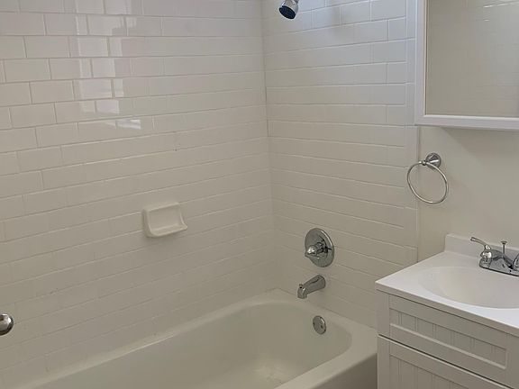Brand new bathtub __, new white tile, new sink and new toilet and beautiful wood flooring. All white bathroom!