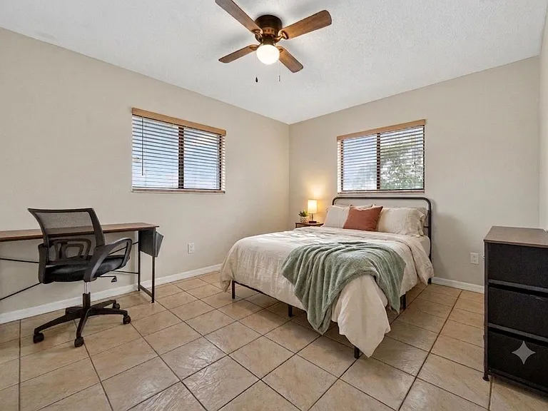 Spacious bedroom with two windows, ceiling fan, tile flooring, and room for a bed plus a dedicated desk/work area.