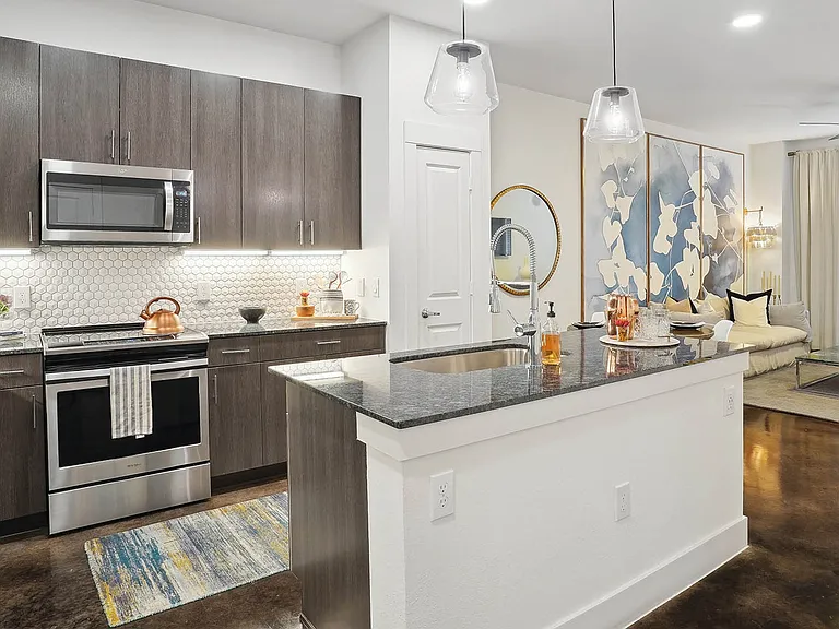 Apartment kitchen with stainless steel appliances, dining and living room with wood-style flooring.