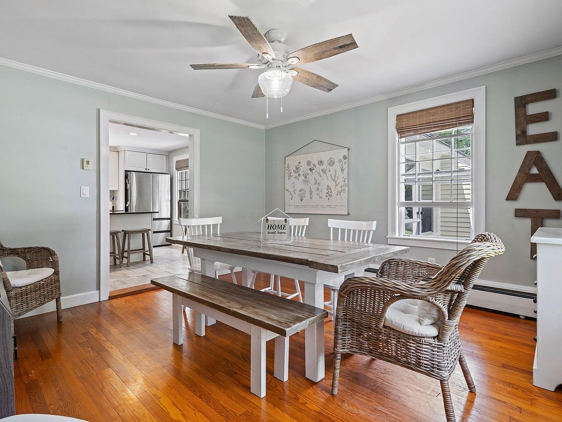 Sunlit dining area with hardwood floors, a farmhouse table, and built-in shelving at 26 Garrison Lane, Hopkinton NH